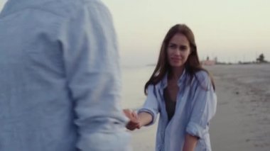 Dişlerinde diş teli olan güzel bir beyaz kız okyanus kıyısında yürüyor ve bir erkeğin elini tutuyor..