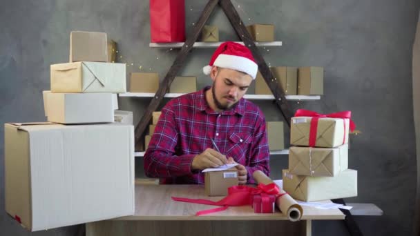 Existenzgründungskonzept für KMU. Ein junger, aufstrebender Unternehmer, Kleinunternehmer, der von zu Hause aus arbeitet, schreibt eine Lieferadresse auf einen Kasten mit einem Stift. — Stockvideo