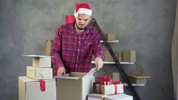 Homem de negócios no chapéu de Natal feliz trabalho vendendo bens on-line em casa. prepara muitos itens para envio. — Vídeo de Stock