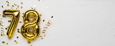 78 numaralı altın folyo balonu. Üzerinde 78 yazan doğum günü veya yıldönümü kartı. Gri beton arka plan..