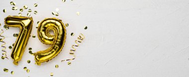 79 numaralı altın folyo balonu. Üzerinde 79 yazan doğum günü ya da yıldönümü kartı. Gri beton arka plan. Yıldönümü kutlaması. Pankart. Boşluğu kopyala