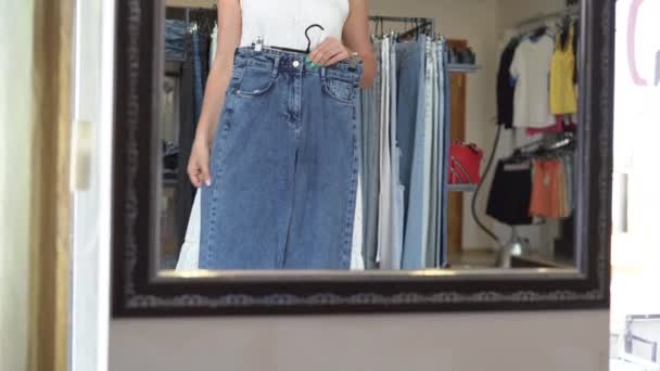 Vêtements, garde-robe, mode, style et concept de personnes - femme heureuse avec un pantalon sur un cintre dans le miroir à la maison. — Video