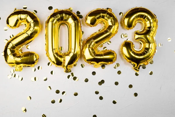 golden foil balloon 2023 New Year. Numbers two thousand twenty three from a foil figure on a gray cement background. Golden confetti and celebration. Copy space