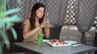 Kafkasyalı bir kadın restoranda oturuyor ve öğle yemeğini akıllı bir telefonla çekiyor..