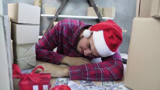 Homem caucasiano em chapéu de Papai Noel adormeceu à mesa enquanto trabalhava cercado por caixas de mercadorias. O conceito de ser sobrecarregado durante a grande venda de Natal de férias. — Vídeo de Stock