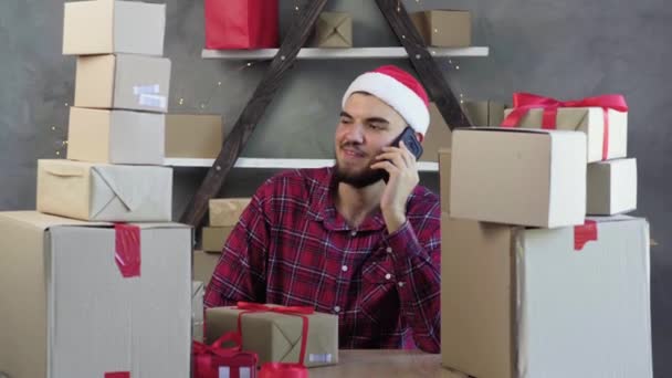 Caucasico maschio piccolo imprenditore si siede a casa ufficio indossando cappello Babbo Natale parlando al telefono. Natale concetto di vendita. — Video Stock