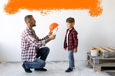 Baba ve oğul evdeki bir odayı yeniliyorlar. Bir adam, oğlu için turuncu lekeli beyaz bir duvara karşı kask takıyor. Tamir ve boyama işi. Metin için yer.