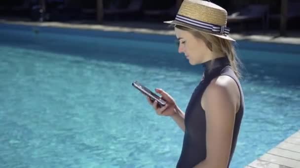 Szczęśliwa kobieta smartfon relaks w pobliżu basenu. Młoda piękna kobieta przewija się przez kanał wiadomości podczas wakacji w ośrodku. — Wideo stockowe