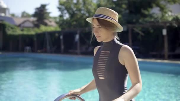 Bella giovane donna entra in piscina, tenendo la scala della piscina. Modello seducente in costume da bagno nero a bordo piscina. concetto di piscina all'aperto. — Video Stock