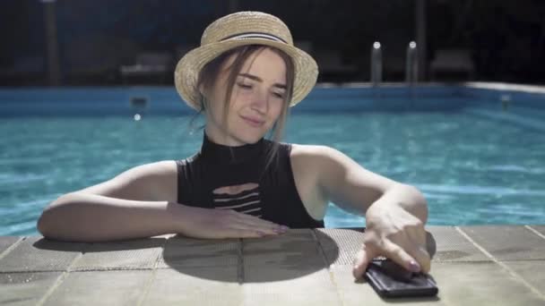 Fröhliche kaukasische Mädchen mit einem Smartphone entspannen im Pool an einem sonnigen Tag, Kopierraum. — Stockvideo
