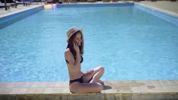 Eine junge Kaukasierin sitzt im Urlaub am Pool und telefoniert. — Stockvideo