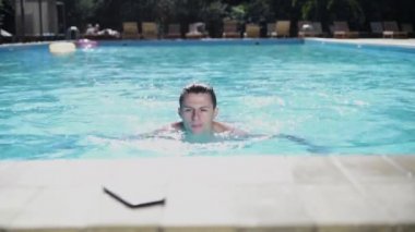 Havuzdaki yakışıklı bir adamın portresi bir otelde tatildeyken kenarına kadar yüzer, bir akıllı telefon alır ve bir video görüşmesi yapar..