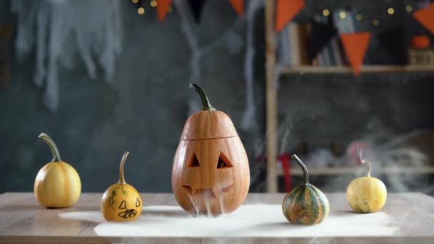 Eine Kürbislaterne auf dem Tisch im Zimmer. Halloween-Kürbis mit Rauch aus seinen Augen und einem gruseligen Lächeln. — Stockvideo