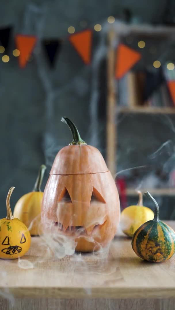 Eine geschnitzte Halloween-Kürbislaterne auf einem Tisch mit gelbem Rauch an der Spitze. aufrecht, Kopierraum. — Stockvideo