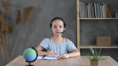 Evde ders çalışan mutlu küçük bir öğrencinin portresi. Gülümseyen küçük kız oturma odasında derslerin keyfini çıkarıyor..