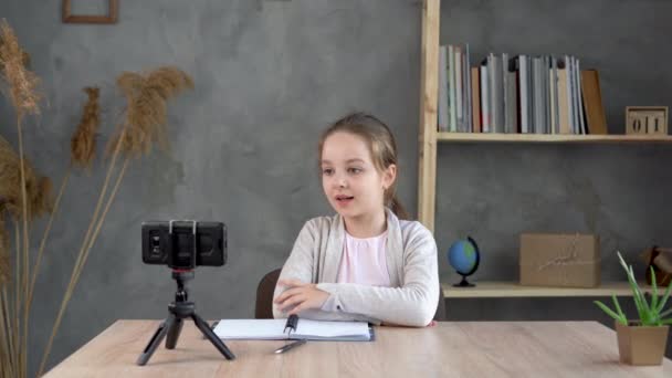 Flicka skolflicka bloggare, influencer skriva vlogging koncept, tala, titta på smartphone på stativ hemma. — Stockvideo