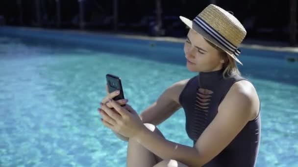 Närbild porträtt vit kvinna i halmhatt sitter nära poolen och blad genom nyhetsflödet. Vila på anläggningen på hotellet. — Stockvideo