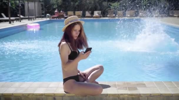 Uma jovem caucasiana senta-se à beira da piscina enquanto está de férias e um estranho nada até ela e quer conhecê-la. conceito de namoro em lugares públicos. — Vídeo de Stock
