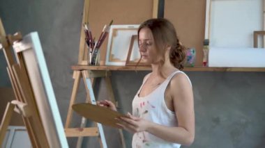 Bir sanat atölyesinde sehpada duran bir kadın ressam tuvale fırçayla resim yapıyor. Genç kız bir palet boyayla resim yapmayı öğreniyor. Sanat tasarımı gerçeklik kavramı