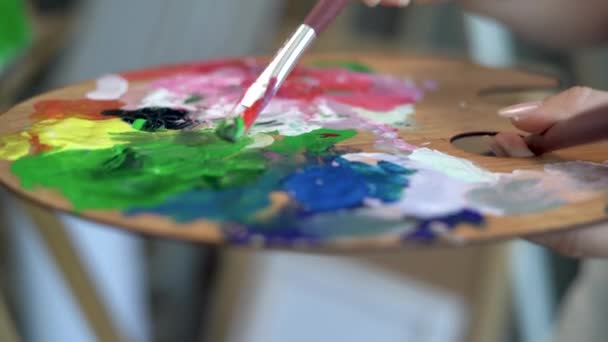Primo piano di una tavolozza di legno con vernici multicolori e una spazzola che mescola la vernice ad olio. Lezione di disegno allo studio. Colorare la compatibilità dei colori per l'artista. — Video Stock