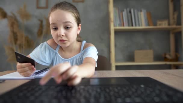 Una joven compradora en línea se sienta a la mesa en casa e introduce un número de tarjeta de crédito en el teclado de un ordenador portátil. Concepto de compras online. — Vídeos de Stock