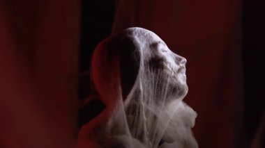 Portrait of Dramatic zombie man trapped in spiderwebs in convulsion on red background. Halloween fantasy horror scene. copy space