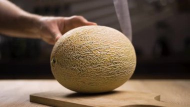 Close-up of ripe melon cutting with sharp knife on wooden cutting board. Cooking vegan fruit food in the kitchen. copy space