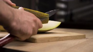 man chopping melons with sharp knife on cutting board in kitchen. vegan food concept. close-up