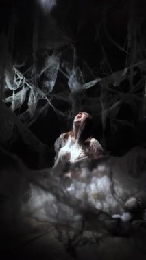 Dramatik gizemli cadı ya da vampir kadın örümcek ağlarında sıkıştı ve karanlık arka planda çığlık atıyor. Cadılar Bayramı korku sahnesi. dikey video