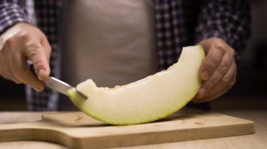 Vejetaryen gıda konsepti. Adam kesme tahtasıyla olgun kavun kabuğunu bıçakla keser. Mevsimlik taze meyve hasadı. yakın plan