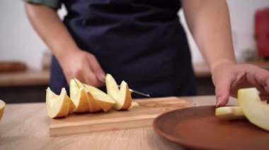 Kadın ellerinin küçük sarı karpuzu doğrama tahtasında bıçakla kestiği yakın plan.