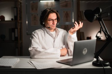 Genç erkek doktor, web kamerasıyla hastaya danışmanlık yapıyor. Teletıp, tele sağlık ve tıp konsepti.