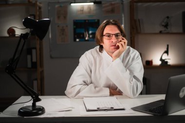 Endişeli doktor, hastanedeki ofisinde gece geç saatlere kadar çalışan tırnak yiyor. Boşluğu kopyala