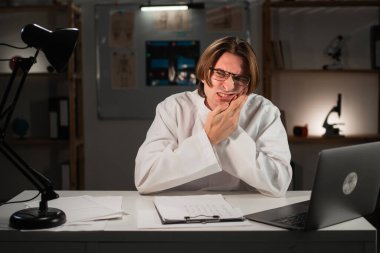 Hastanede gece vardiyasında çalışırken diş ağrısı çeken erkek doktorun portresi. Diş problemi, diş ağrısı. Diş sağlığı konsepti.