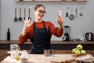 Önlüklü genç bir kadın evdeki mutfakta cep telefonuyla konuşuyor. Sağlıklı diyet yaşam tarzı kavramı