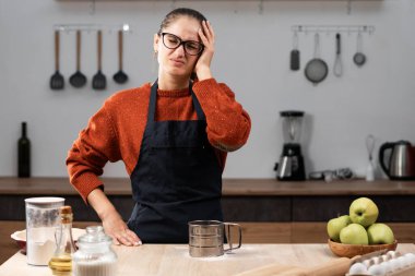 Genç ev hanımı fırıncı kadın mutfakta baş ağrısı ve migren çeken önlük giyiyor. Tıp, sağlık ve Yemek pişirme konsepti