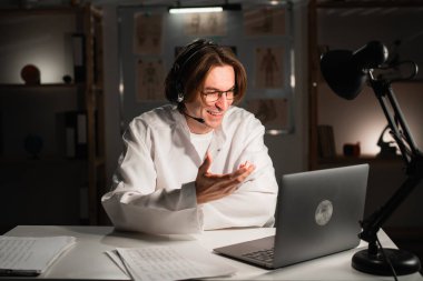 Genç erkek doktor, web kamerasıyla hastaya danışmanlık yapıyor. Teletıp, tele sağlık ve tıp konsepti.