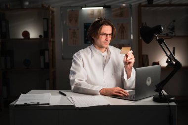 Doktor adamın elinde kredi kartı var. Finansal işlemler yapıyor ya da sigorta ödemelerini hastanede gece vardiyasında yapıyor. Tıbbi hizmetler kavramları.