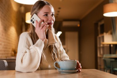 Mutlu bir kadın cep telefonuyla arkadaşlarını arar kahvesini içer kahvecide oturup uzaktan çalışır. Bağımsız ofis. Boşluğu kopyala
