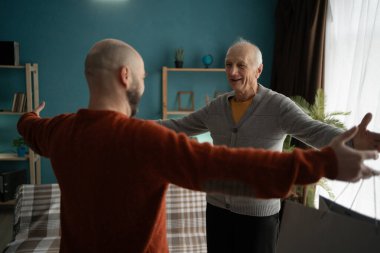 Olgun bir adam evdeki oturma odasında kolları açık bir şekilde oğlunu selamlıyor. Boşluğu kopyala