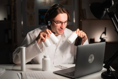 Elinde ilaç şişesi olan genç bir doktor hastane ofisinde gece vardiyasında çalışıyor. teletıp ve tele sağlık kavramı