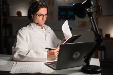 Teletıp konsepti. Genç psikolog, hastanede gece vardiyası sırasında online danışmanlık yapan hastayı dinliyor. Boşluğu kopyala