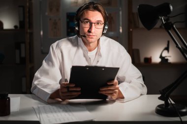 Gözlüklü bir erkek doktor, ofisinde gece vardiyasında çalışan dizüstü bilgisayarla çevrimiçi video görüşmesi yapıyor. Teletıp konsepti. POV