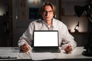 Genç doktor, boş ekranlı dizüstü bilgisayarın gece vardiyasında çalıştığını gösteriyor. Sağlık web sitesi. Boşluğu kopyala