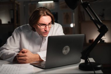 Hastanede gece vardiyasında dizüstü bilgisayar başında çalışırken gözlük kullanan genç bir doktor görme sorunu yaşıyor. Görme sorunları. Boşluğu kopyala