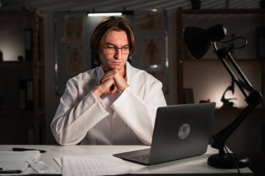 Hastanede gece vardiyası sırasında bilgisayarla video konferansı yapmaya odaklanmış bir doktor. Hastayla çevrimiçi konuşma. Boşluğu kopyala