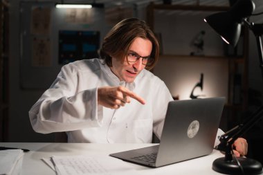 Tartışmacı öfkeli doktor hastanede gece vardiyası sırasında dizüstü bilgisayarla video konferansı yapıyor. Hastayla çevrimiçi konuşma. Boşluğu kopyala