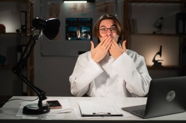 Şok olmuş pratisyen doktor masa başında sürpriz bir şekilde oturuyor ve ağzı kapalı bir şekilde hastane ofisinde gece vardiyasında çalışarak ödüllü bir iş alıyor. Boşluğu kopyala