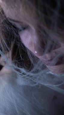 Close-up of woman face emerging from delicate spiderweb cocoon symbolizing gentle awakening and transformation, eyes opening in atmospheric artistic scene with metaphorical butterfly rebirth concept.