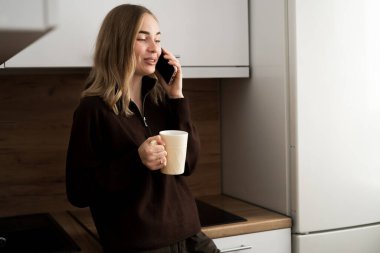 Modern Mutfağında Akıllı Telefonla Konuşan Gülümseyen Genç Kadın. Boşluğu kopyala